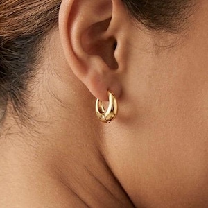 Gold-colored hoop earrings, 12mm in size, are displayed on an ear. The earrings have a smooth, polished finish and a classic, rounded shape. The image is a close-up, highlighting the jewelry's design and shine.