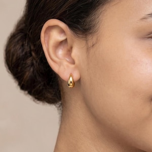 Gold-colored hoop earrings, 8mm in size, are displayed on a right ear. The earrings have a smooth, polished finish and a classic, rounded shape. The image is a close-up, highlighting the jewelry's design and shine.