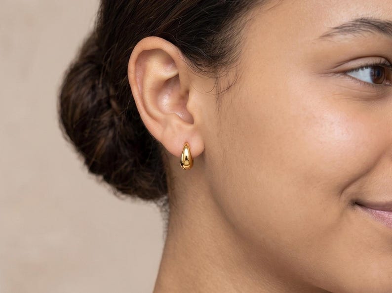 Gold-colored hoop earrings, 8mm in size, are displayed on a right ear. The earrings have a smooth, polished finish and a classic, rounded shape. The image is a close-up, highlighting the jewelry's design and shine.