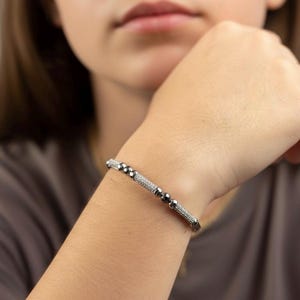 A silver bangle bracelet with small round stones and a row of smaller stones. On a person's wrist