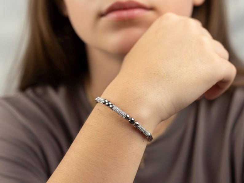 A silver bangle bracelet with small round stones and a row of smaller stones. On a person's wrist