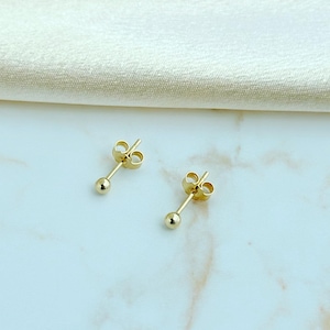 May include: A pair of gold ball stud earrings featuring a small, polished spherical bead attached to a thin post with a matching butterfly clutch backing. The earrings have a bright, reflective metallic finish and a simple, classic design.