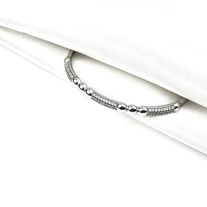 May include: A silver bracelet with a row of small round beads and a row of sparkling stones.