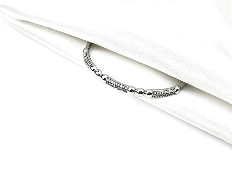 May include: A silver bracelet with a row of small round beads and a row of sparkling stones.
