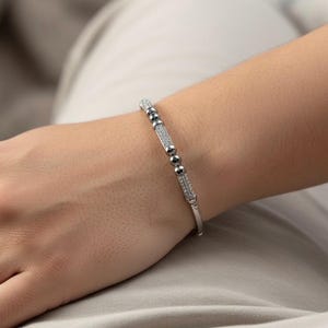 A silver bangle bracelet with small round stones and a row of smaller stones. On a person's wrist