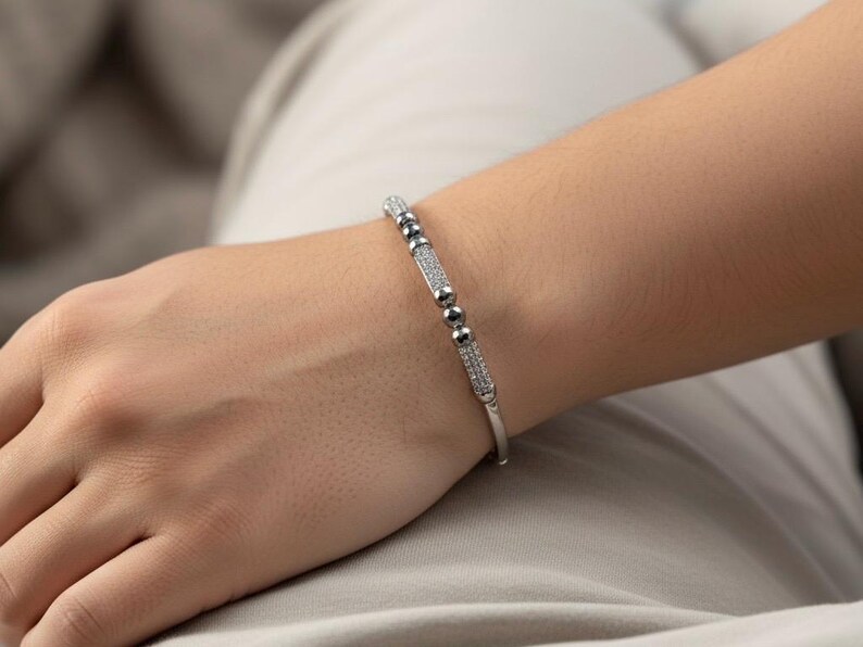 A silver bangle bracelet with small round stones and a row of smaller stones. On a person's wrist