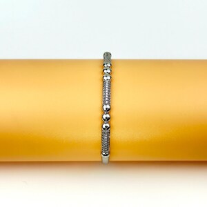 May include: A silver bracelet with small round beads and a row of sparkling stones.