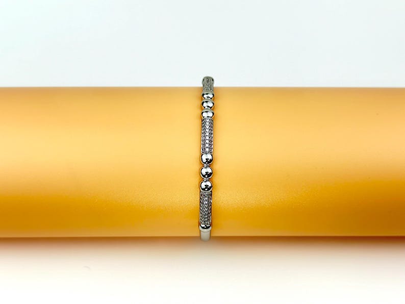 May include: A silver bracelet with small round beads and a row of sparkling stones.