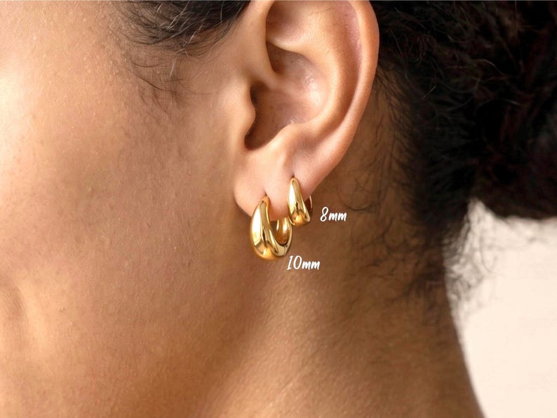 Gold-colored hoop earrings, 8mm and 10mm in size, are displayed on an ear. The earrings have a smooth, polished finish and a classic, rounded shape. The image is a close-up, highlighting the jewelry's design and shine.