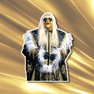 Puede incluir: Una pegatina que presenta a una persona con un elaborado disfraz. Tiene la cara dorada, maquillaje de ojos negro y pelo largo y rubio. El atuendo es negro y dorado con adornos de plumas blancas. El fondo es un degradado dorado.