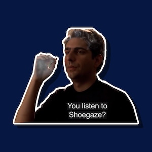 May include: A man with dark hair and a black shirt is looking at the camera and holding a cigarette. He is exhaling smoke. The text "You listen to Shoegaze?" is written below him.