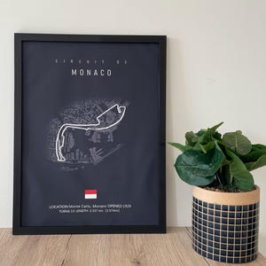 Può includere: Stampa incorniciata del circuito di Monaco, con tracciato bianco su sfondo blu scuro. Il testo "CIRCUIT DE MONACO" è in alto. Il testo in basso recita "LOCATION: Monte Carlo, Monaco OPENED:1929 TURNS: 19 LENGTH: 3.337 km".