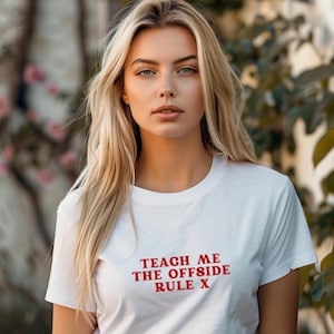 Op de afbeelding: Wit T-shirt met rode tekst die "Teach me the offside rule x" luidt.