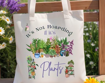 May include: A cream-colored canvas tote bag featuring a colorful graphic of various potted plants and the text "It's Not Hoarding if it's Plants" in dark blue and purple lettering. The design includes multiple indoor plants in pots.