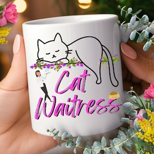 May include: White ceramic mug with a black cat illustration and the words "Cat Waitress" in pink script. The design includes a cartoon cat, a waitress, and a bowl of food.