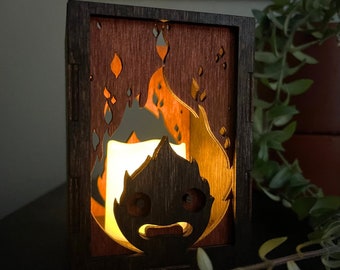 May include: A wooden candle holder with a cutout design of a flame with a face. The candle holder is lit and the flame is glowing.