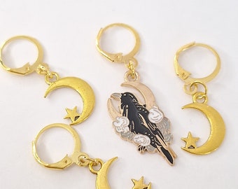 May include: Three gold hoop earrings with crescent moon and star charms. One charm features a black raven with white clouds.