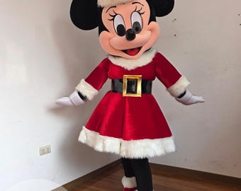Puede incluir: Un disfraz de mascota de un personaje con grandes orejas negras, que lleva un vestido de terciopelo rojo con ribete de piel sintética blanca, un cinturón negro con hebilla dorada, guantes blancos y un gorro de Papá Noel rojo a juego.