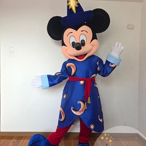 以下が含まれることがあります： 魔法使いの格好をした漫画のネズミのキャラクターの全身マスコットコスチューム。キャラクターは金色の星が付いた青いとんがり帽子、三日月と星の模様が入った青いローブ、赤い帯、そして大きな青い靴を身に着けています。