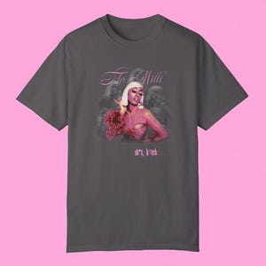 May include: A dark gray t-shirt with a pink graphic of a woman with a pink feather boa and the text "The Milli" and "sh*t, b*tch".