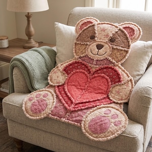 Könnte beinhalten: Ein gestepptes, bärenförmiges Zierkissen mit Patchwork-Design in Rosa-, Braun- und Cremetönen. Der Bär hat ausgefranste Kanten und hält ein großes, mehrschichtiges rotes Herz in der Mitte, mit aufgestickten Gesichtszügen.