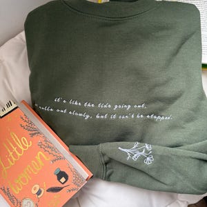 May include: A green sweatshirt with the quote "It's like the tide going out. It pulls out slowly, but it can't be stopped." embroidered on the back. The sweatshirt has a small embroidered flower design on the sleeve.