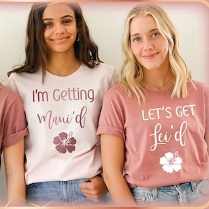 May include: Three women wearing t-shirts with text and a floral graphic. Two shirts say "LET'S GET Lei'd" with a white hibiscus flower. The centre shirt says "I'm Getting Maui'd" with a hibiscus flower.