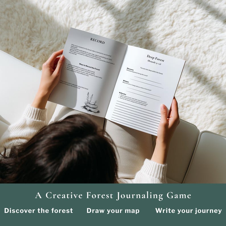 May include: A person holding open a journal with the text "RECORD" and "Deep Forest" visible. The journal is part of "A Creative Forest Journaling Game". The person is sitting on a white couch with a fluffy white blanket.