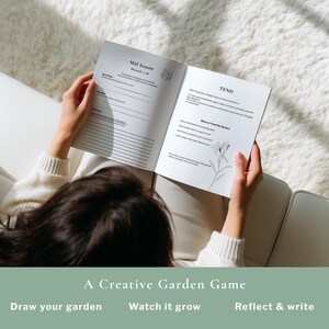 May include: A person holding open a journal with the text "Mid Season" and "TEND" visible. The journal is part of "A Creative Garden Game" and includes prompts to "Draw your garden", "Watch it grow", and "Reflect & write".
