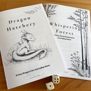 Könnte beinhalten: Zwei offene Bücher mit Schwarz-Weiß-Illustrationen und Text. Ein Buch trägt den Titel "Dragon Hatchery" mit einer Drachenillustration. Das andere Buch trägt den Titel "Whispering Forest". Zwei Würfel befinden sich im Vordergrund. Die Bücher tragen die Aufschrift "A Cozy Dragon Care Journaling Game" und "A Cozy Forest Exploration Journaling Game."