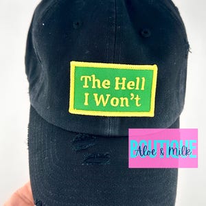 May include: Black distressed baseball cap with a green and yellow patch that reads "The Hell I Won't".