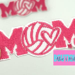 Pu&ograve; includere: Toppa in feltro rosa da stirare con la parola "MOM" in cuciture bianche. Una pallavolo bianca con un cuore rosa &egrave; centrata tra la "M" e la "O".