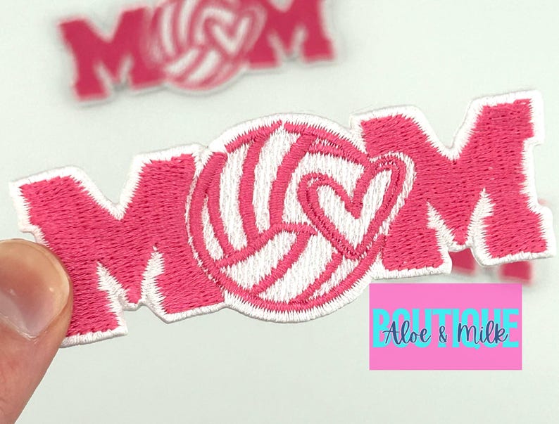 Pu&ograve; includere: Toppa in feltro rosa da stirare con la parola "MOM" in cuciture bianche. Una pallavolo bianca con un cuore rosa &egrave; centrata tra la "M" e la "O".