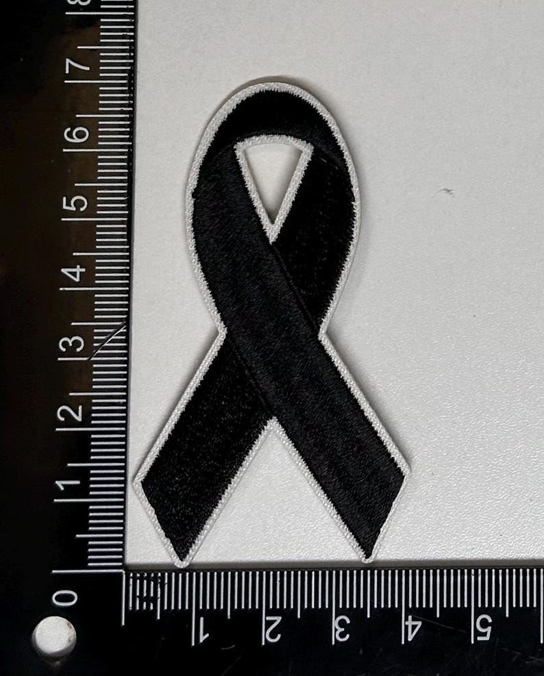 May include: Black ribbon patch with white stitching, measuring approximately 2 inches wide and 3 inches long.