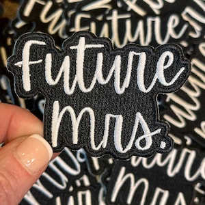 May include: Black and white embroidered patch with the text "Future Mrs." in a cursive font. The patch has a black background with white stitching and a scalloped edge. The patches are scattered.