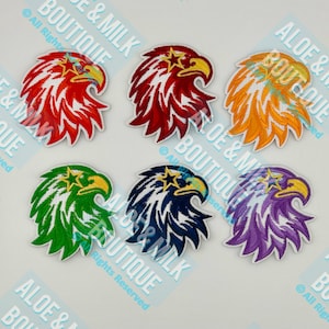 May include: Six embroidered eagle head patches in various colors: red, burgundy, orange, green, navy, and purple. Each patch features a yellow beak and a star on the head. The patches are on a white background.
