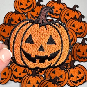 May include: A collection of orange felt pumpkin patches with black embroidered faces. The pumpkins are arranged in a circle with one pumpkin in the center.