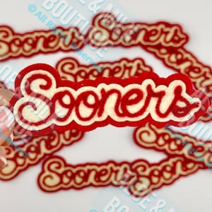 May include: Red and white "Sooners" word cutouts. The word "Sooners" is in a cursive font with a red border and white interior. Several cutouts are visible, with one in focus.