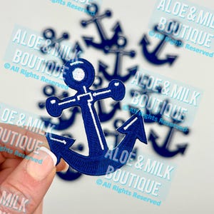 May include: A close-up of a blue anchor patch with white stitching. The anchor is surrounded by other anchor patches, all with the text "Aloe & Milk Boutique" and "All Rights Reserved".