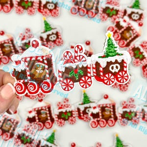 May include: Embroidered Christmas train patches with red, white, and brown details. Each train car features candy cane accents, gingerbread men, and Christmas trees. The patches are designed with a festive holiday theme.