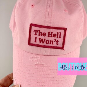 May include: Pink distressed baseball cap with a red patch that says "The Hell I Won't".