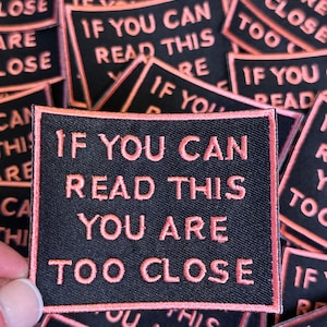 May include: A black fabric patch with pink stitching that reads "If you can read this you are too close".