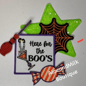 May include: A set of four Halloween-themed iron-on patches. The patches feature a witch's broom, a spiderweb, a candy, and a square patch with the text "Here for the BOO'S" and a cartoon witch with a martini glass.