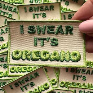 May include: A close-up of a green and white embroidered patch that reads "I swear it's oregano".