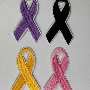 May include: Four embroidered ribbon patches in different colors: purple, black, yellow, and pink. Each ribbon is white-outlined and has a classic ribbon shape.
