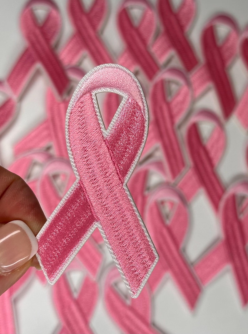 May include: A close-up of a pink ribbon with a white outline. The ribbon is made of fabric and has a textured surface. The ribbon is a symbol of breast cancer awareness.