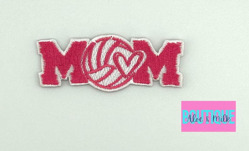 Pu&ograve; includere: Toppa in feltro rosa con la parola "MOM" in lettere bianche bordate. Una pallavolo bianca con un cuore rosa &egrave; al centro della toppa.
