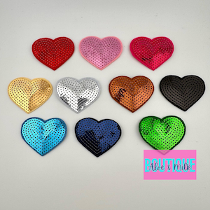May include: Ten heart-shaped sequins in various colors, including red, pink, gold, silver, brown, black, blue, and green. The sequins are arranged in a circle on a white background. The text "Boutique Aloe & Milk" is visible in the bottom right corner.