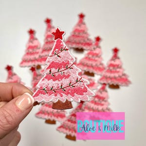 May include: A set of pink Christmas tree iron-on patches with white embroidery and red accents. The patches are approximately 2 inches tall.