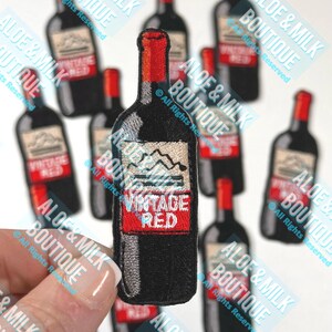 May include: A close-up of a black and red embroidered iron-on patch of a wine bottle with the text "Vintage Red".